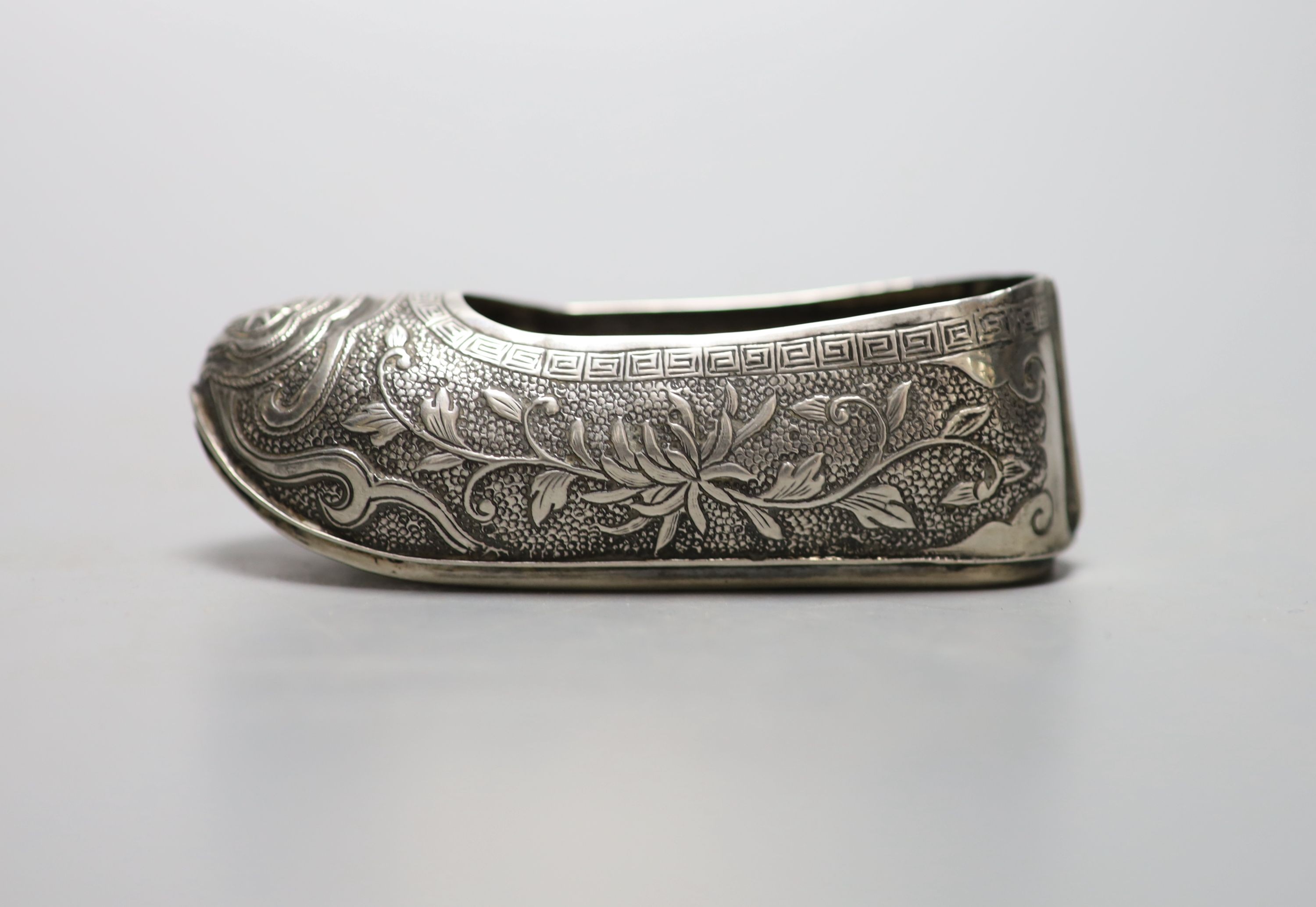 An early 20th century Chinese engraved white metal pin cushion, modelled a s a shoe, (lacking cushion), maker HC, 85mm.